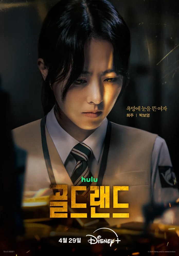 Close-up of a focused female character from a drama, wearing a uniform with a serious expression, illuminated by soft light, with the title '골드랜드' prominently displayed.