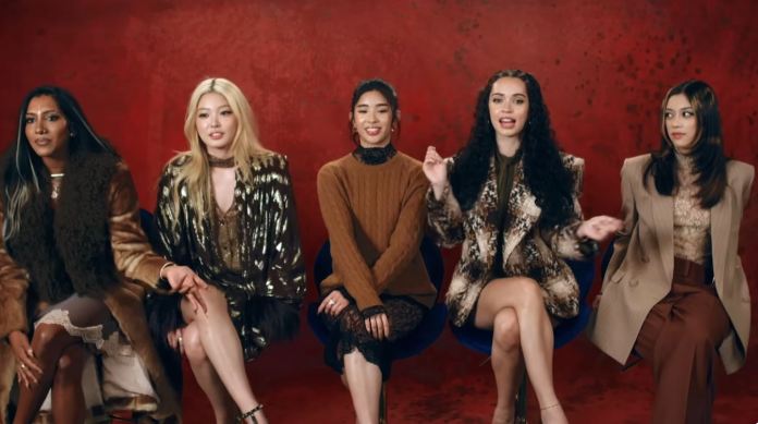 KATSEYE members sitting in front of a red background, each wearing stylish outfits and engaged in conversation.