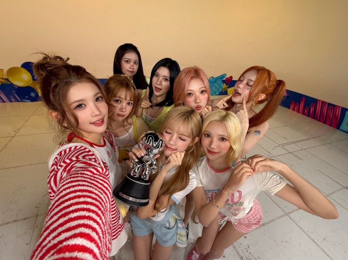 H2H posing together for a selfie, celebrating with an award trophy. They are wearing casual clothes and smiling, with a colorful background and playful expressions.