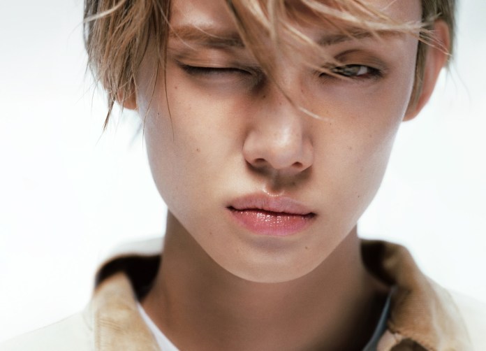 Close-up portrait of Yeonjun with light-colored hair, winking with a serious expression against a soft-focus background.