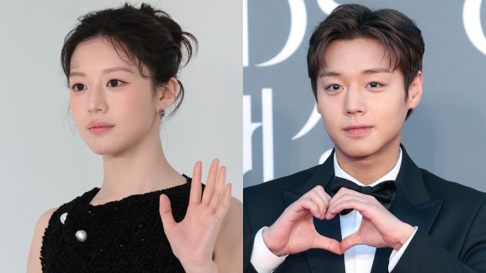 Go Youn-jung in a black dress with a pearl detail waves gently, while Park Ji-hoon in a tuxedo makes a heart shape with his hands against a gray backdrop.