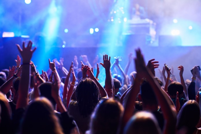 A crowd of concertgoers with raised hands enjoying a live performance, illuminated by colorful stage lights.