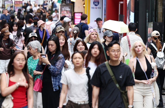 A busy urban street bustling with a diverse crowd of pedestrians, including people of various ages and styles, some wearing hats and carrying bags, capturing the lively atmosphere.