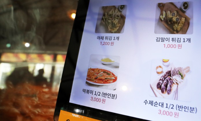A digital menu displaying various Korean dishes, including fried vegetables, kimbap, tteokbokki, and sliced sausages, with prices listed in Korean won.