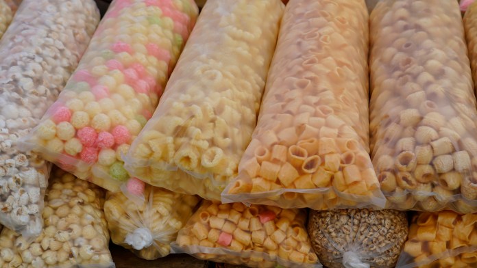 Colorful bags of various snacks, including popcorn and puffed cereal, neatly arranged in a market display.