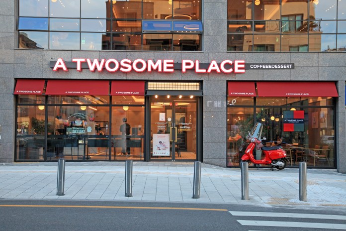 A storefront of a coffee and dessert shop named 'A Twosome Place,' featuring large glass windows, a red awning, and a vintage red scooter parked outside.