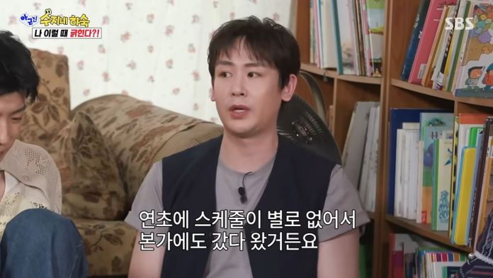 Nichkhun sitting on a couch in a cozy room filled with bookshelves. 