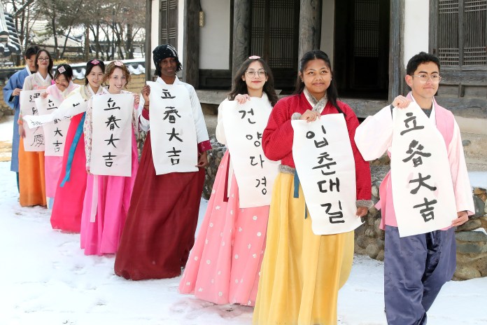 A diverse group of individuals dressed in traditional Korean hanbok, walking in a line on snowy ground while holding large banners with Korean text.