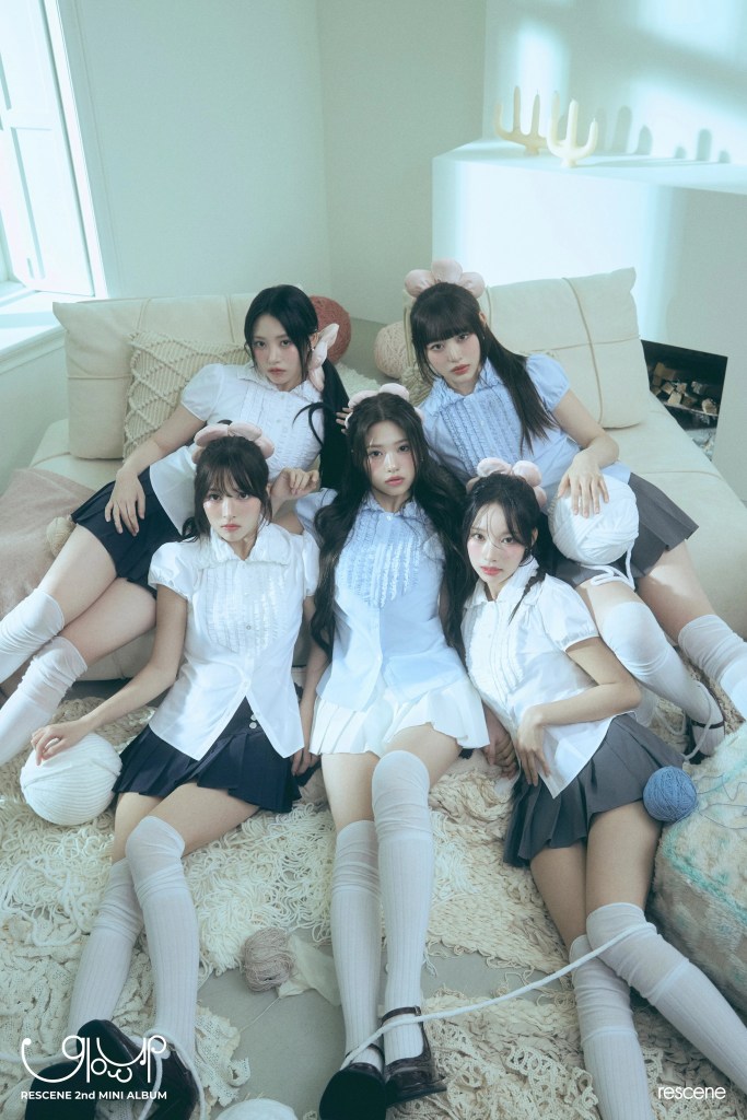 RESCENE dressed in school-themed outfits, sitting together on a couch adorned with soft textiles and yarn. They have long hair and wear knee-high socks, with some accessorized with plush headbands.