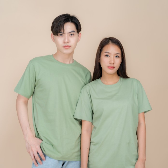 A man and woman are standing side by side, both wearing plain green t-shirts, against a light beige background.