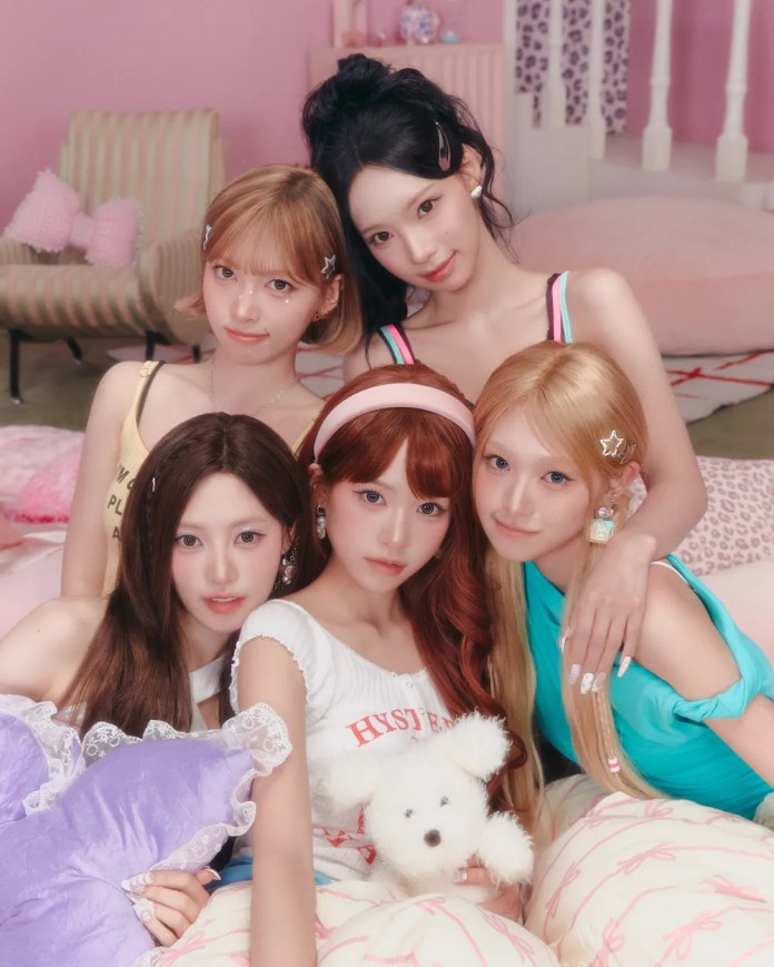 RESCENE posing together in a pastel-themed room, surrounded by soft furnishings and holding a stuffed toy. They are dressed in colorful, casual outfits and are styled with hair accessories, creating a playful and cozy vibe.