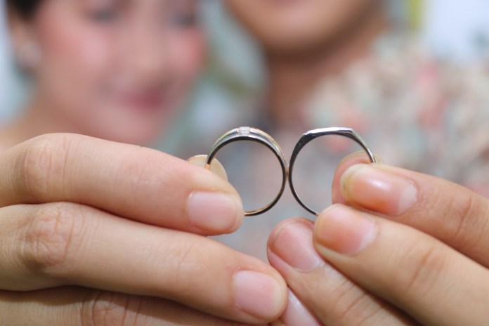 Close-up of two wedding rings held by a couple, with a blurred background.