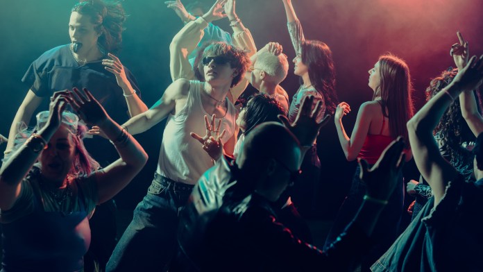 A lively group of diverse individuals dancing energetically in a club setting, with colorful lights and a vibrant atmosphere.