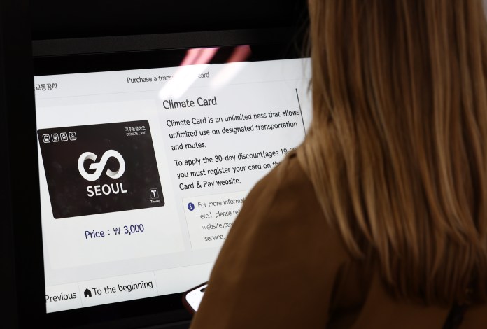 A person viewing a digital screen displaying information about the Climate Card, an unlimited pass for public transportation in Seoul, including its price and application details.