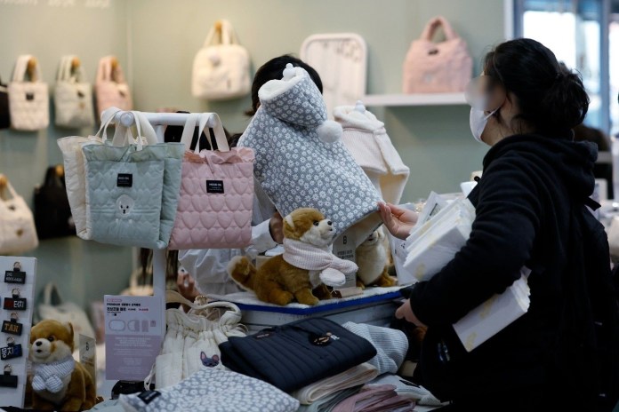 A shopper browsing through a variety of colorful bags and stuffed animals at a retail store, with several bags displayed on the wall behind.