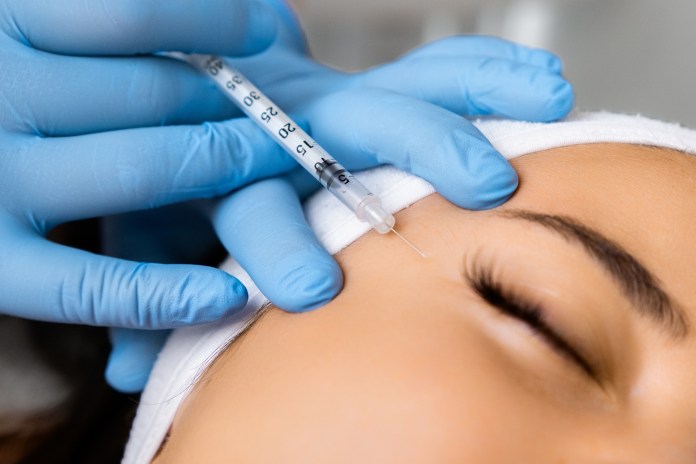 A close-up image of a person receiving an injection on the skin, with a gloved hand holding a syringe near the face, showcasing a focus on the treatment area.