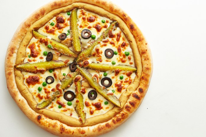 A gourmet pizza topped with sliced pickles, black olives, and green peas on a golden crust with melted cheese.