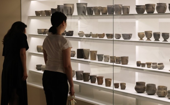 Two visitors examining a display case filled with various clay pots and artifacts in a museum.