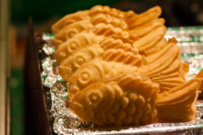 A row of golden fish-shaped pastries displayed on a silver tray.