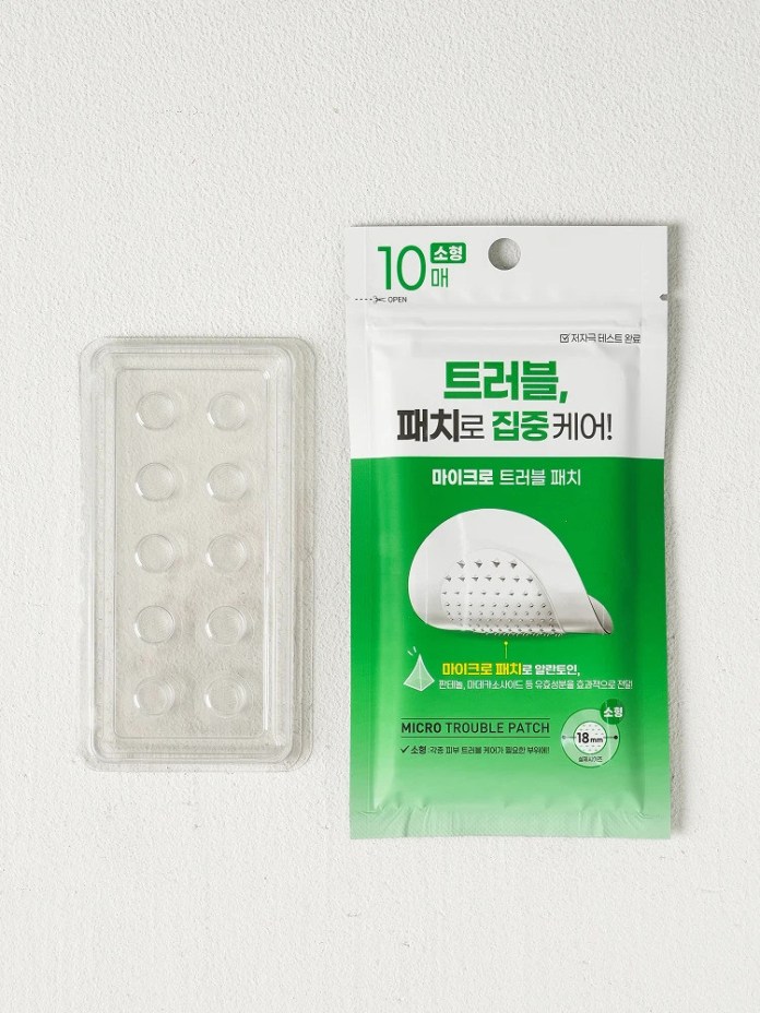 A package of micro trouble patches, featuring a green design with the text 'MICRO TROUBLE PATCH' and information in Korean. Next to the package is a transparent plastic tray containing several circular patches.
