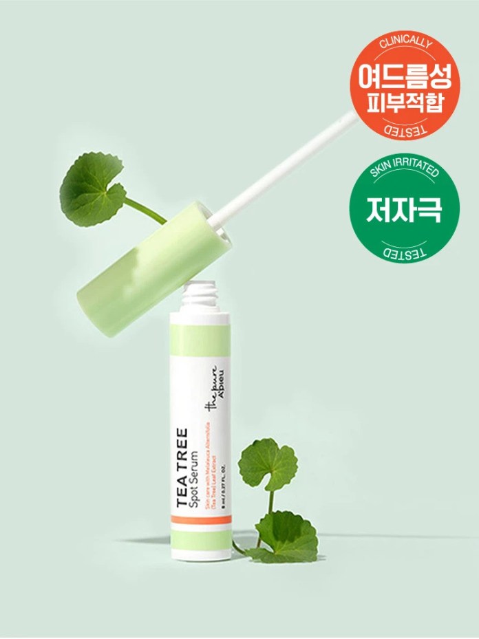 A Tea Tree Spot Serum bottle with a green cap, partially open, showcasing a brush applicator. The background is a soft green color, and a small leaf is placed beside the bottle.