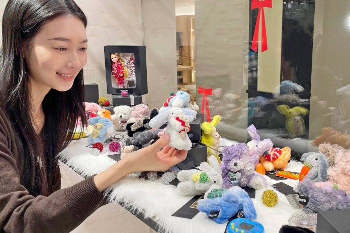 A young woman smiling while holding a stuffed animal, surrounded by various colorful plush toys on a display table.