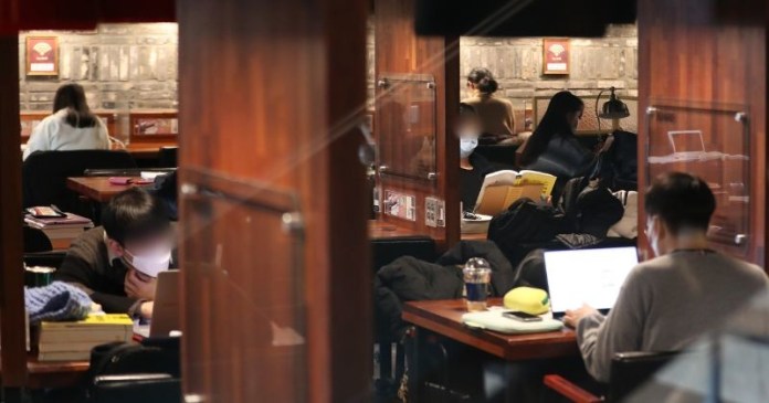 A cozy study space featuring students working at wooden tables, some using laptops and textbooks, in a softly lit environment.