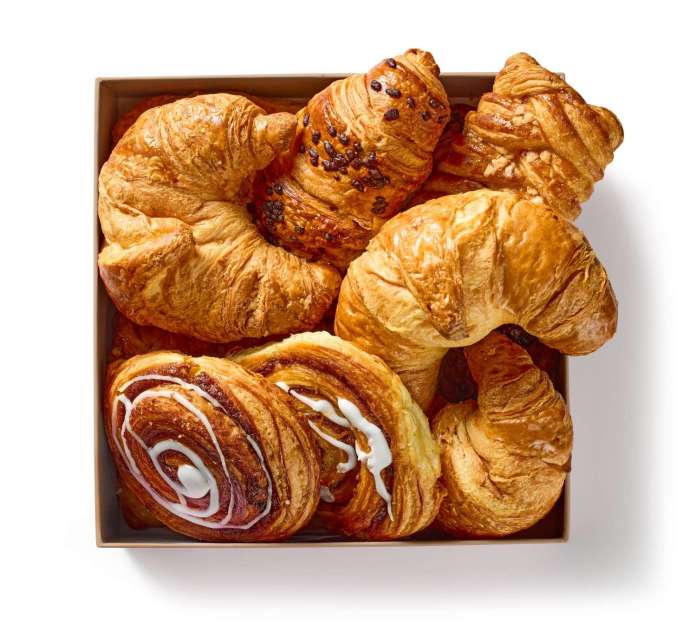 A variety of fresh pastries including croissants, chocolate croissants, and cinnamon rolls in a decorative box.