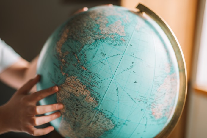 A person’s hand is touching a globe, highlighting North America and the Atlantic Ocean, with a blurred background.