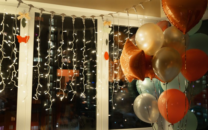 Colorful balloons and fairy lights decoratively arranged by a window.