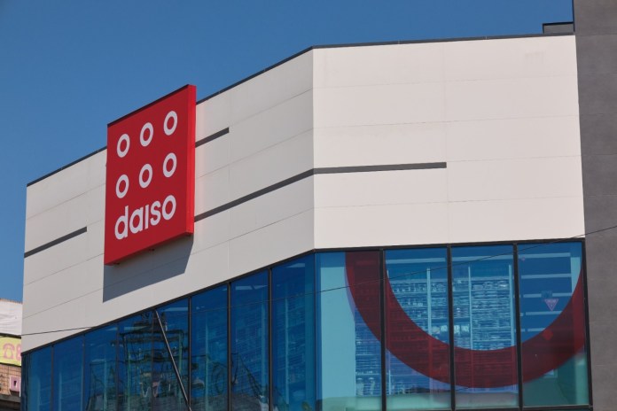 Exterior view of a Daiso storefront featuring a large red sign with the Daiso logo and modern architectural design.