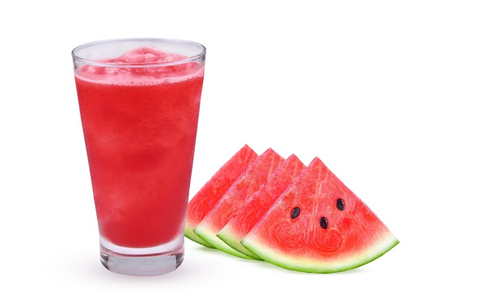 A glass of red watermelon juice next to slices of fresh watermelon on a white background.