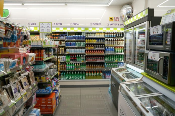 A view of the interior of a convenience store, showcasing various beverage options on shelves, including milk, soda, and coffee, with snacks and personal care items on display.