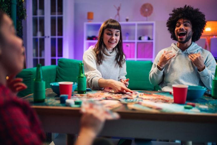 Group of friends enjoying a board game night, laughing and interacting at a cozy table with drinks and snacks.