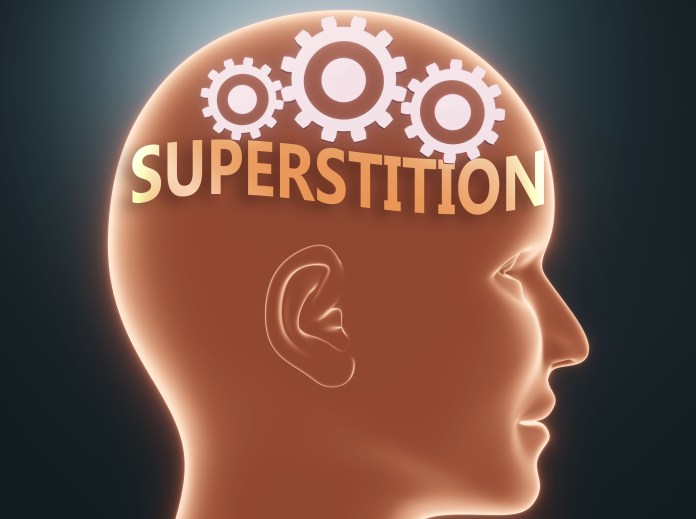 A graphic representation of a human head in profile with the word 'SUPERSTITION' displayed above it, accompanied by cogwheel illustrations.