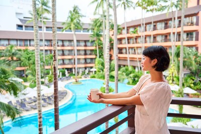 A guest enjoys a peaceful moment with a cup of coffee on a balcony overlooking the pool and resort at Courtyard by Marriott Phuket, Patong Beach Resort