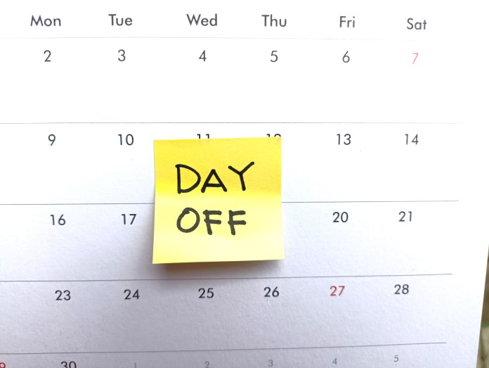 A calendar page with a yellow sticky note reading 'DAY OFF' attached to it.