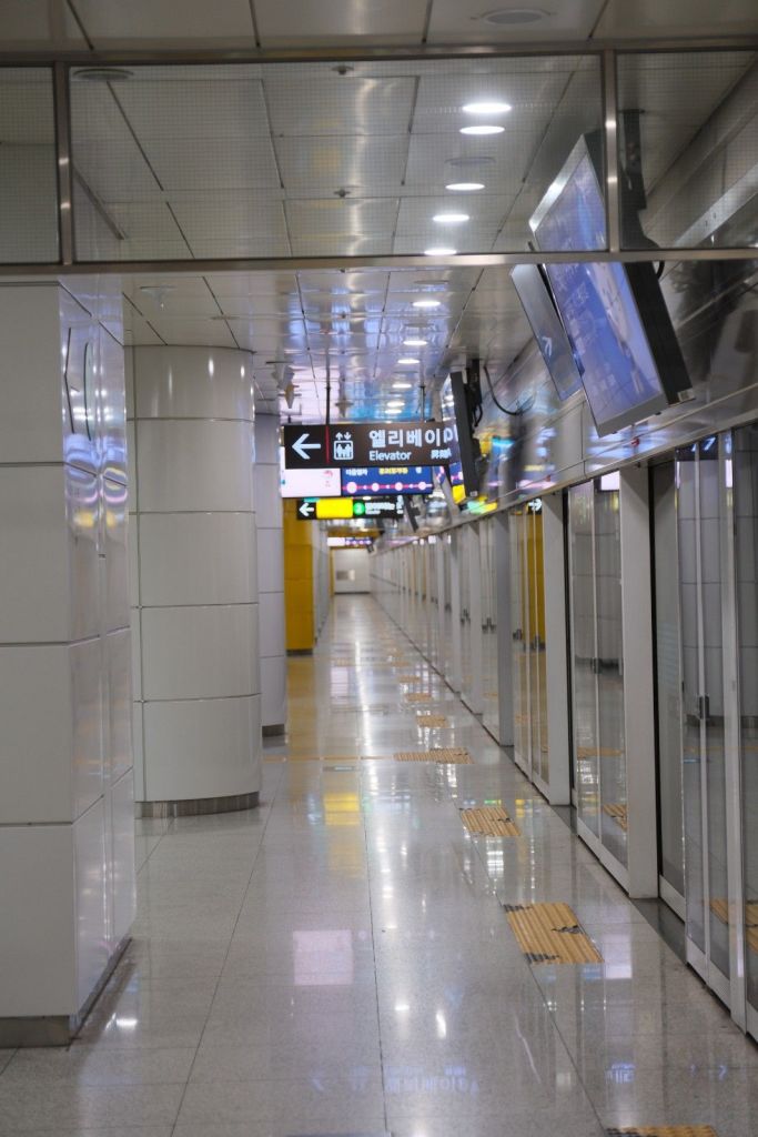 A view of a modern subway station corridor featuring bright lighting, digital signage indicating directions, and smooth polished floors.