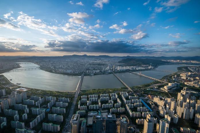 Aerial view of a cityscape featuring rivers, bridges, and buildings, with a sunset sky in the background.