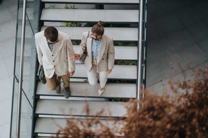 Aerial view of a man and woman in business attire walking up a modern staircase, engaged in conversation.