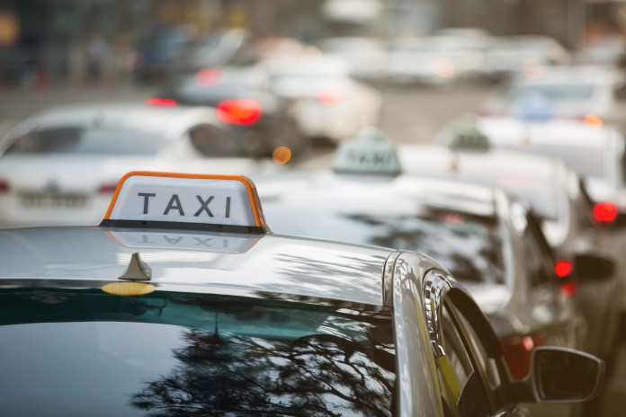 Close-up of a taxi with a 'TAXI' sign on top, surrounded by other cars in traffic.