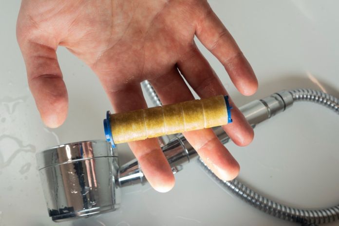 A hand holding a small, cylindrical tool wrapped in tape, with a blue end, placed near a shiny faucet and hose.