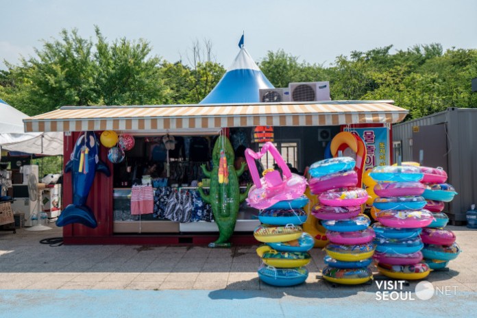A vibrant outdoor stall selling beachwear and accessories, featuring inflatable pool toys like flamingos and dolphins, and colorful inner tubes stacked nearby.