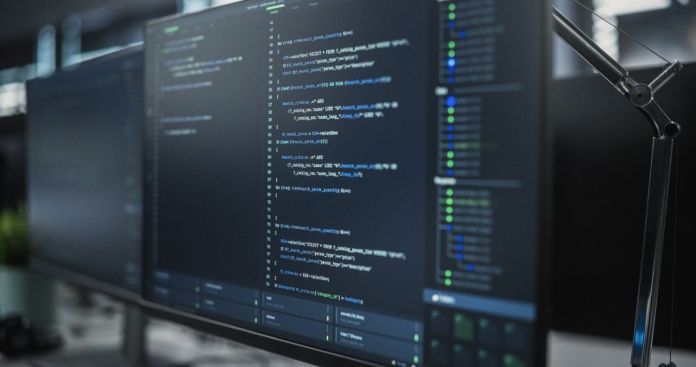 Close-up of a computer screen displaying lines of code in a programming environment, with multiple screens visible in a modern workspace.
