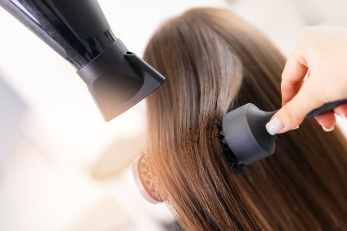 A close-up of a person blow-drying hair while using a round brush.