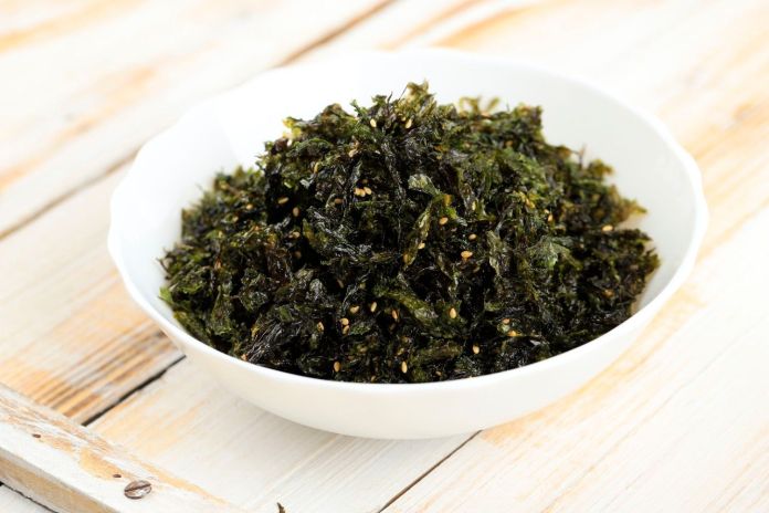 A bowl of crispy seaweed snacks garnished with sesame seeds, placed on a wooden surface.