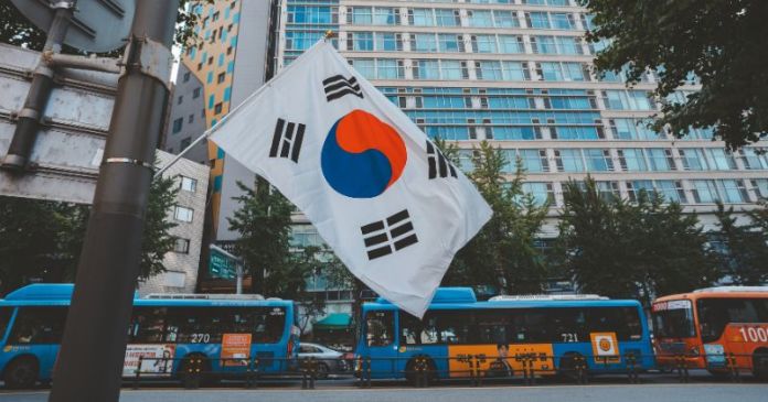 South Korean flag waving in front of city buses and a modern building.