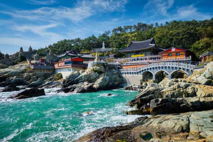 Scenic coastal view featuring traditional Asian architecture, rocky cliffs, and turquoise waters.