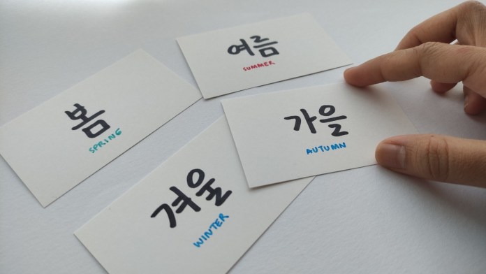 A hand touching a card labeled '가을' (Autumn) alongside cards labeled with the seasons in Korean: '봄' (Spring), '여름' (Summer), and '겨울' (Winter).