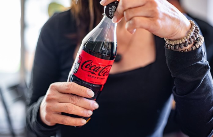 A person holding a bottle of Coca-Cola Zero Sugar in a casual setting.